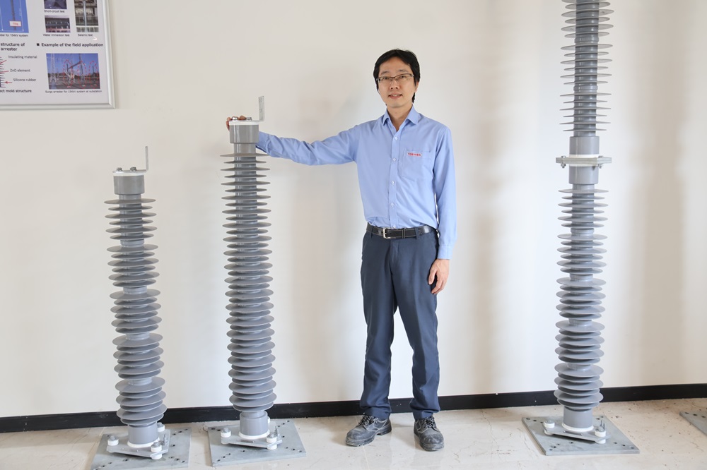 製造する避雷器と小林氏。避雷器には、東芝の強みである酸化亜鉛素子が使用されている