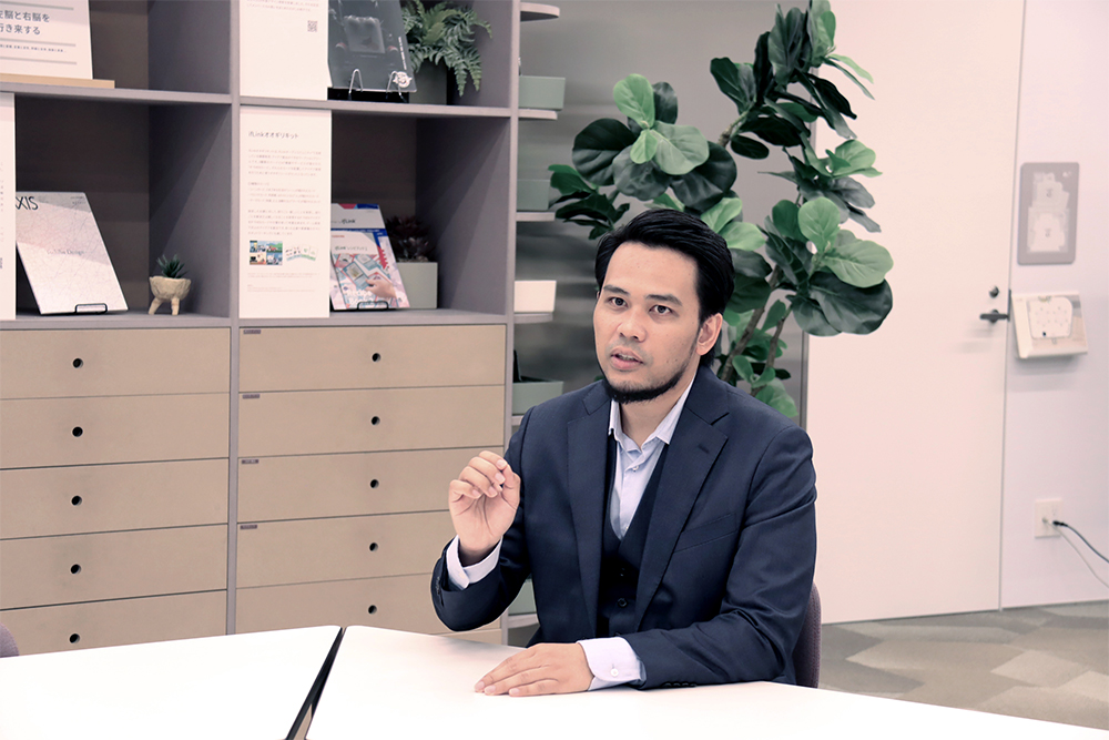 Angga Suherman speaking during an interview at a conference table in a modern office environment.